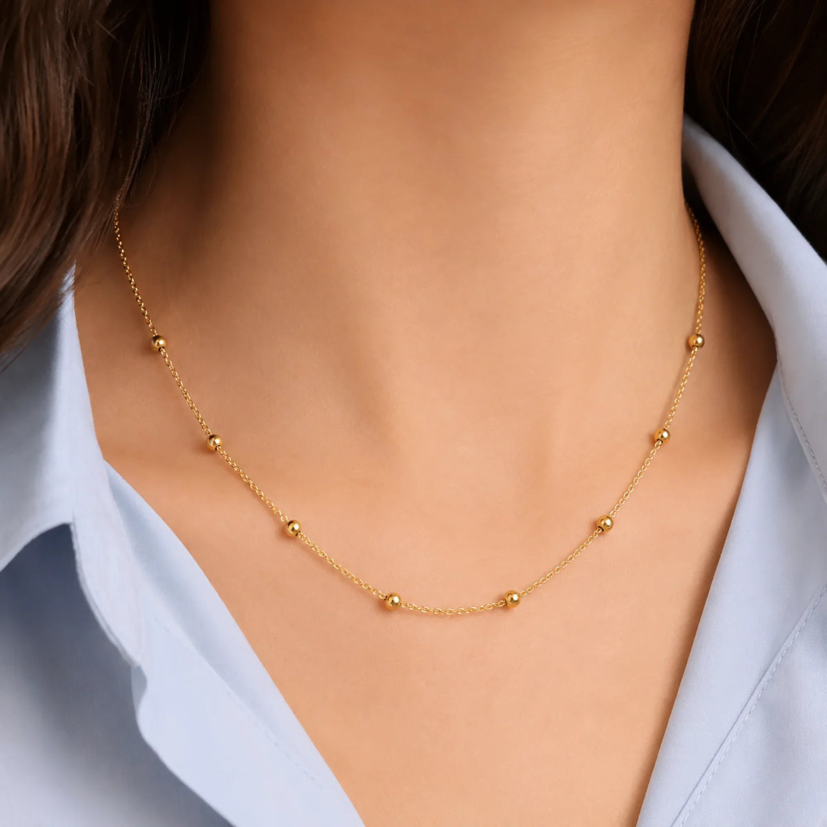 Woman wearing a Lucche 14K gold beaded necklace over a light blue shirt